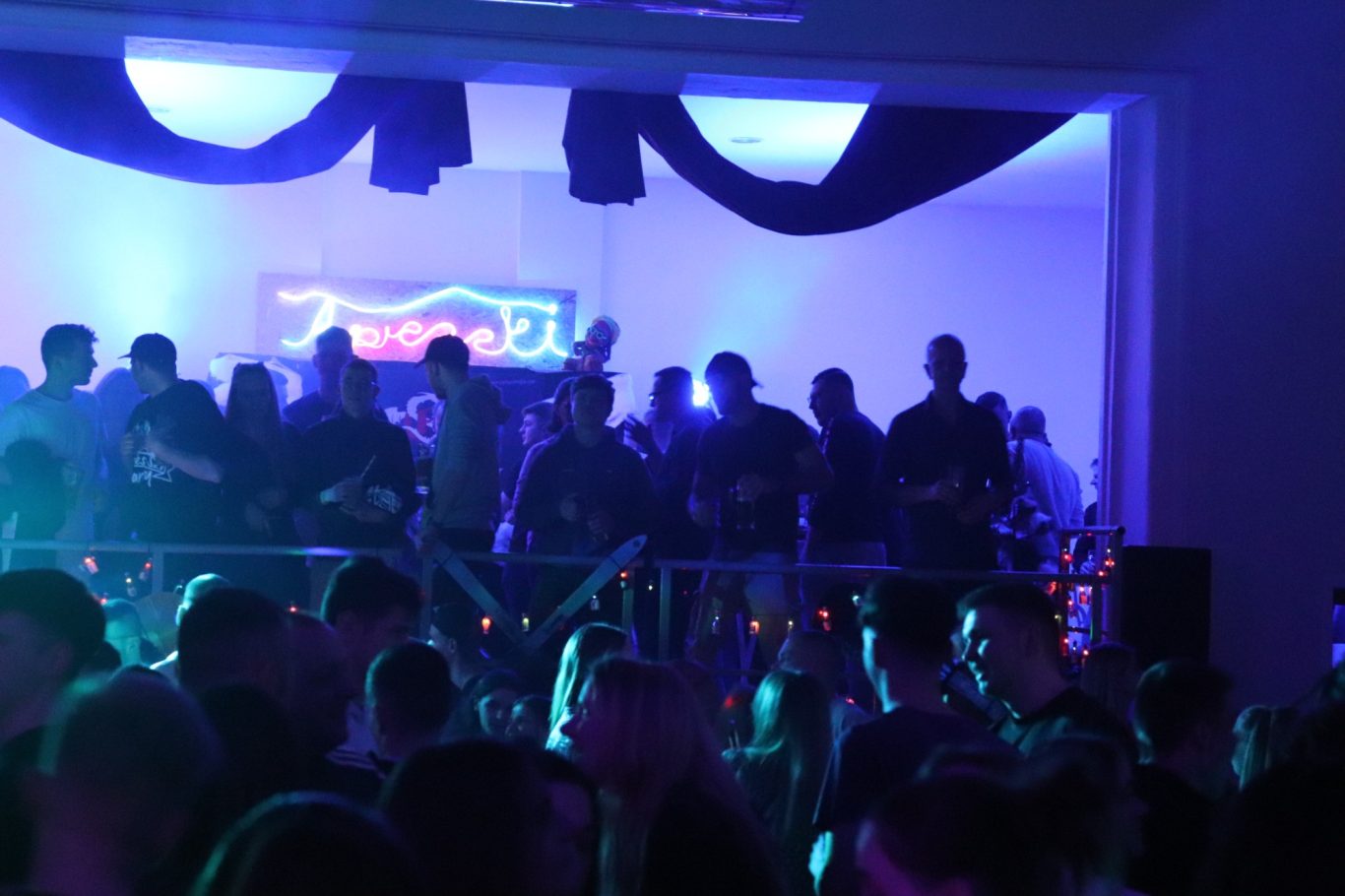 Bunte Lichter und Menschenmenge bei einer Feier mit Musik und Tanz.