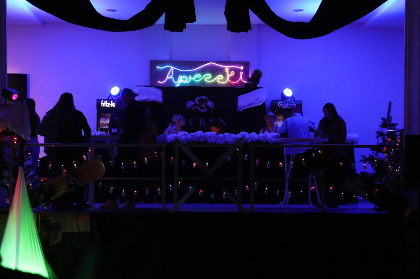 Bunte Lichter und Silhouetten von Personen auf einer festlich dekorierten Bühne.