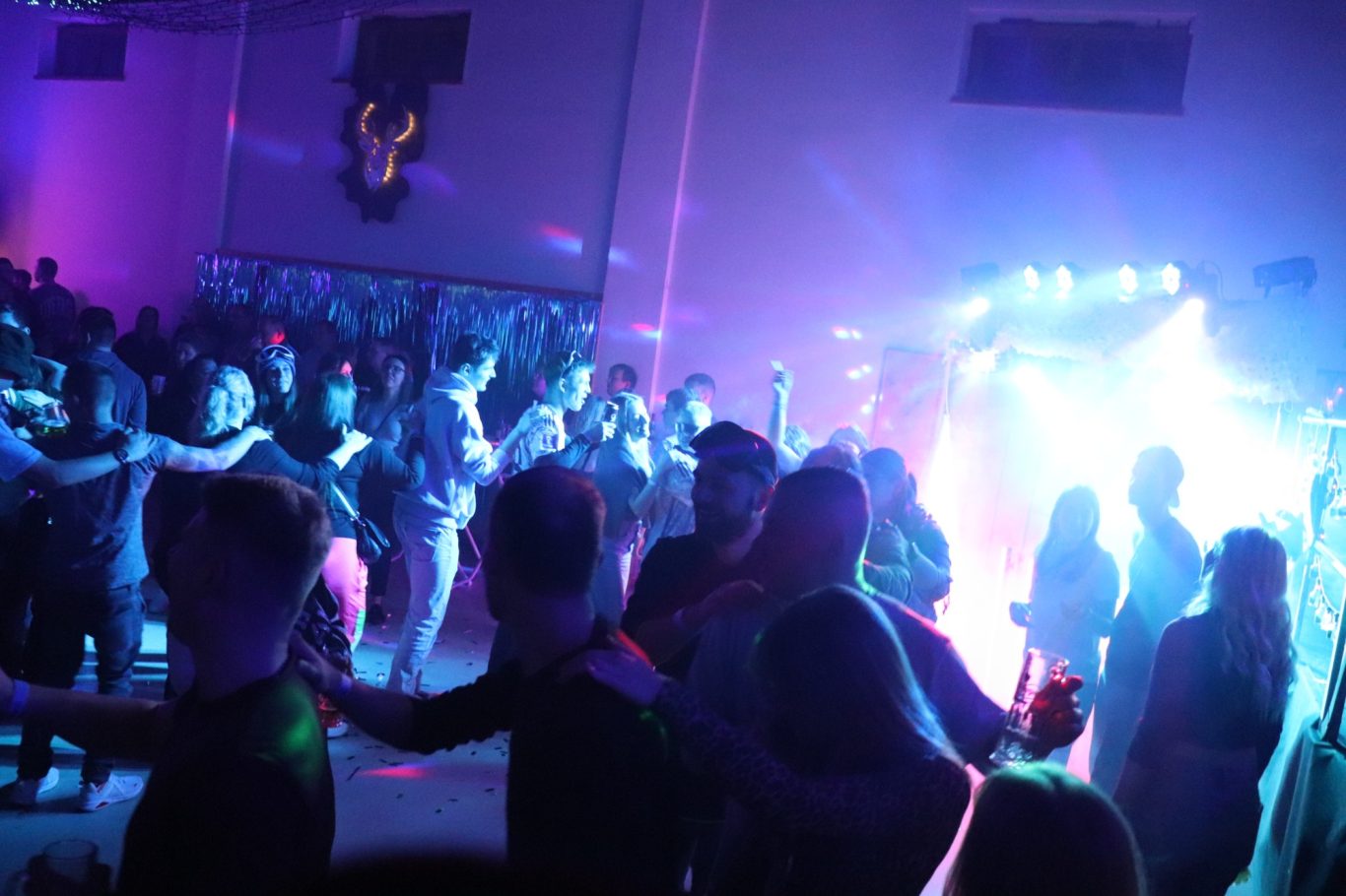Menschen tanzen in einer farbenfrohen Partyatmosphäre mit Lichtern und Musik.