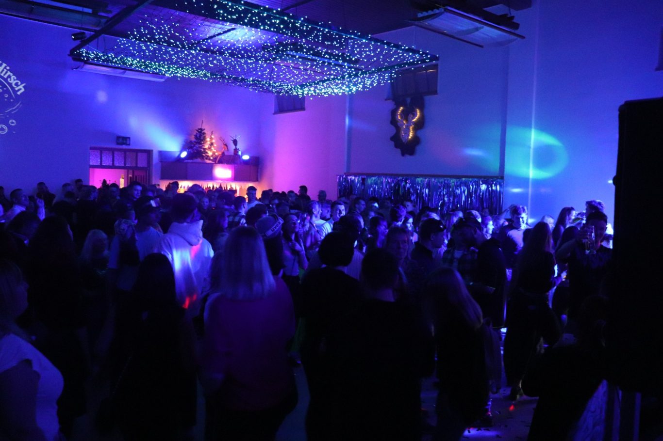 Farbenfrohe Disco-Atmosphäre mit tanzenden Menschen und einem DJ im Hintergrund.